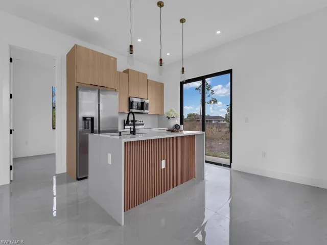 Kitchen with a center island with sink, light stone counters, stainless steel appliances, modern cabinets, and hanging light fixtures