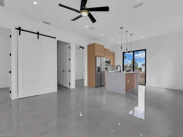 Kitchen featuring a barn door, a kitchen island with sink, ceiling fan, decorative light fixtures, and modern cabinets