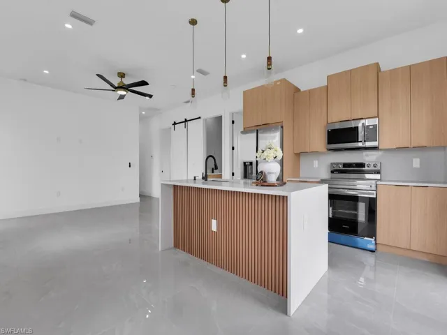 Kitchen with a barn door, an island with sink, stainless steel appliances, modern cabinets, and hanging light fixtures