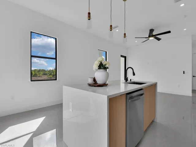 Kitchen with modern cabinets, light stone counters, an island with sink, finished concrete floors, and dishwasher