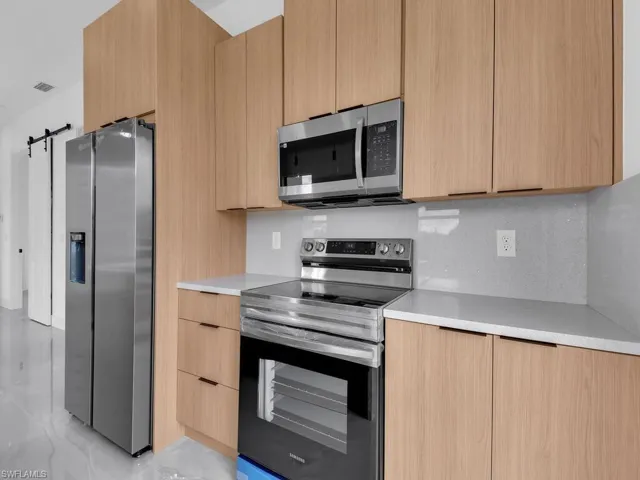 Kitchen featuring stainless steel appliances, a barn door, modern cabinets, light wood finish cabinetry, and tasteful backsplash