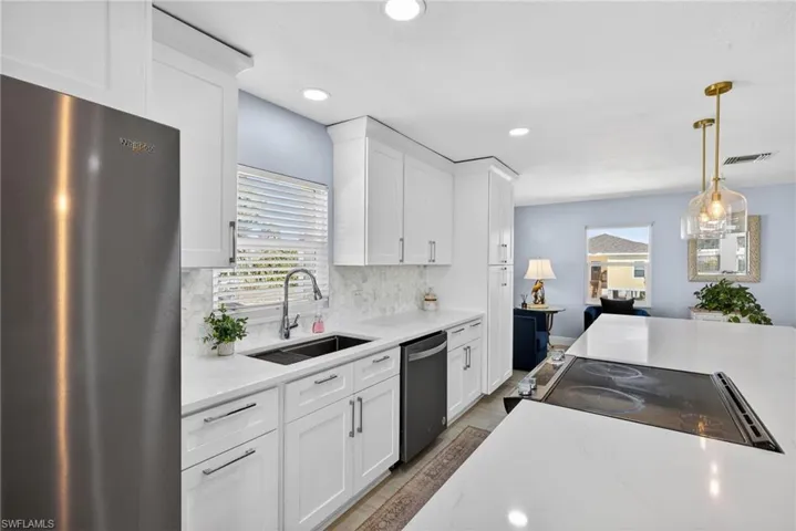 Kitchen with stainless steel appliances, white cabinets, hanging light fixtures, and tasteful backsplash