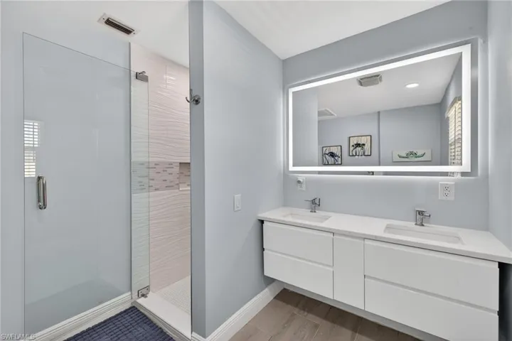 Full bathroom with a stall shower, double vanity, and light wood-type flooring