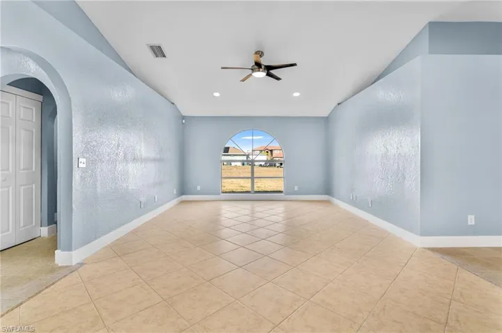 Empty room featuring arched walkways, a textured wall, a ceiling fan, light tile patterned floors, and vaulted ceiling
