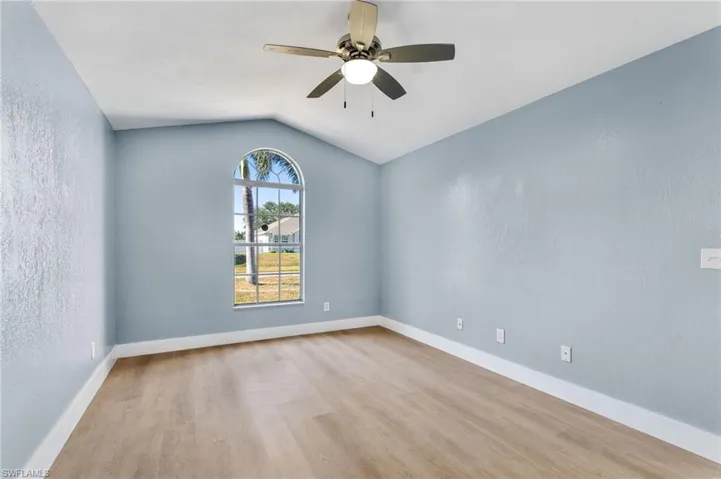Spare room featuring a textured wall, ceiling fan, light wood-type flooring, and lofted ceiling