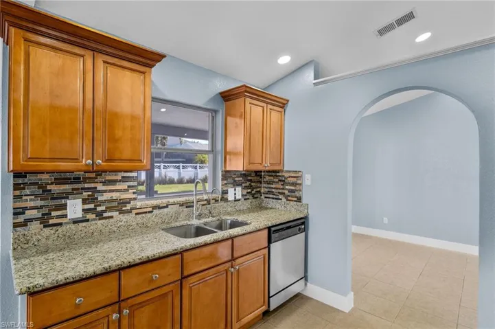 Kitchen with light stone counters, dishwasher, wood finish cabinetry, arched walkways, and light tile patterned floors