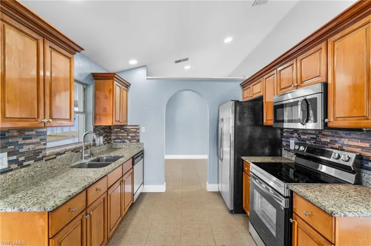 Kitchen featuring tasteful backsplash, light stone countertops, arched walkways, stainless steel appliances, and wood finish cabinetry