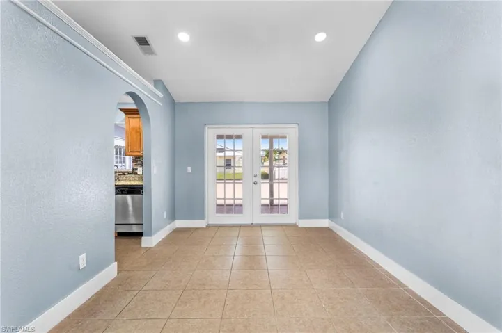 Spare room with arched walkways, french doors, light tile patterned floors, a textured wall, and recessed lighting