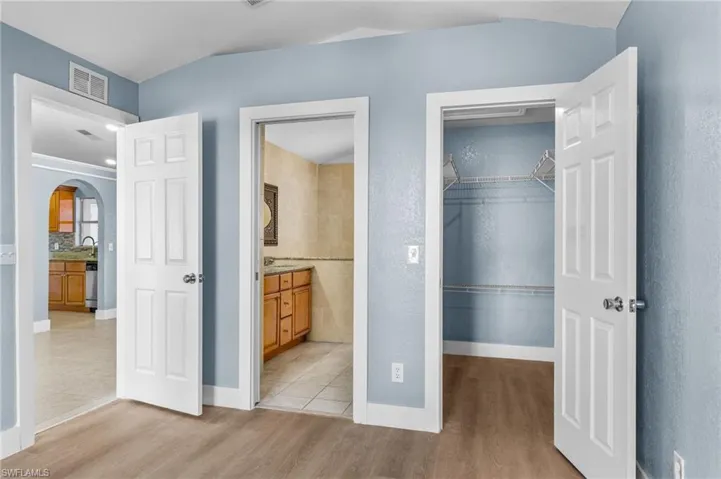 Unfurnished bedroom with a spacious closet, arched walkways, light wood-style flooring, and connected bathroom