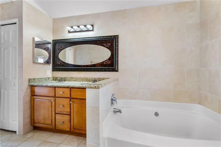 Bathroom with a closet, vanity, tile walls, a garden tub, and light tile patterned floors