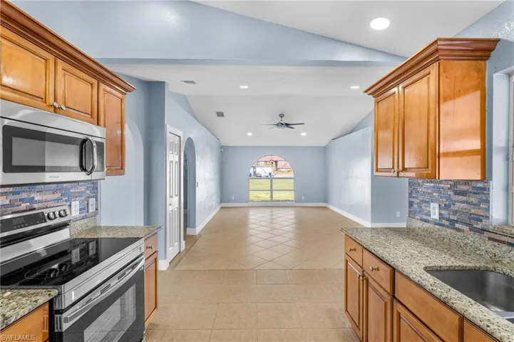 Kitchen featuring backsplash, stainless steel appliances, light stone counters, vaulted ceiling, and open floor plan
