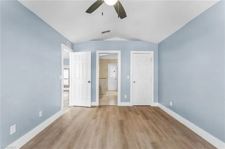 Unfurnished bedroom with a closet, vaulted ceiling, light wood-style floors, a textured wall, and ceiling fan