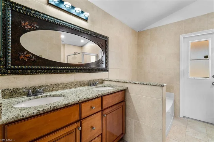 Full bath featuring tile walls, double vanity, vaulted ceiling, a garden tub, and light tile patterned flooring