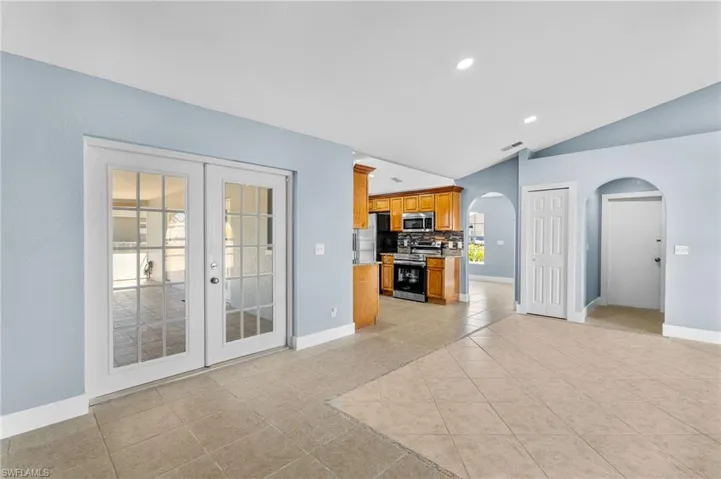 Unfurnished living room with arched walkways, light tile patterned floors, recessed lighting, vaulted ceiling, and french doors