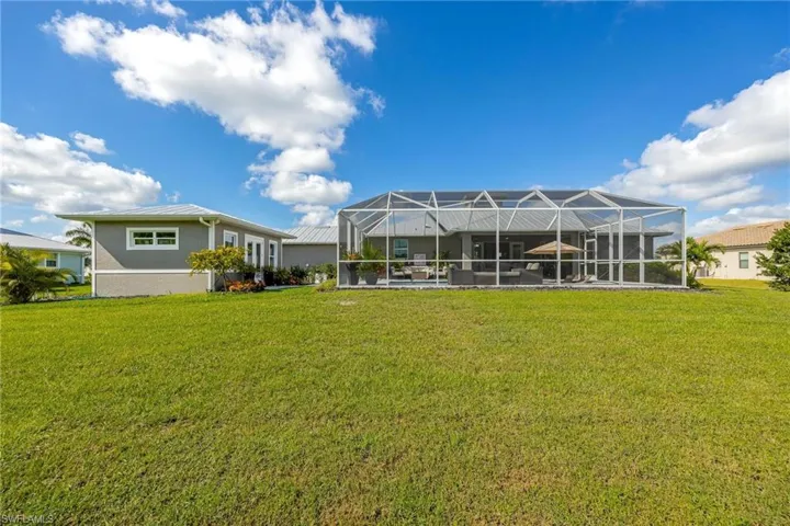 Back of property featuring a lanai and a sprawling green lawn.
