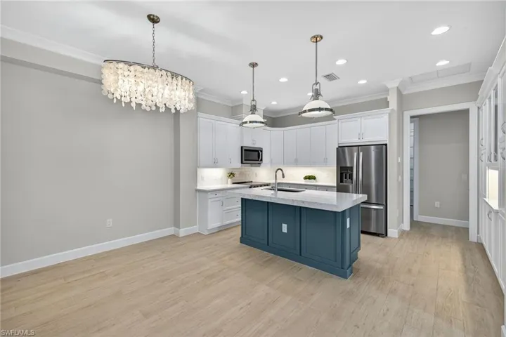 Kitchen featuring appliances with stainless steel finishes, white cabinetry, a kitchen island with sink, decorative light fixtures, and crown molding