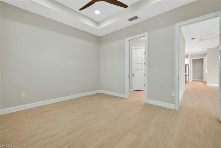 Empty room with light wood-style flooring, a raised ceiling, recessed lighting, and a ceiling fan