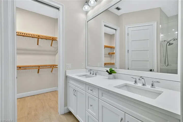 Full bath featuring double vanity, a walk in closet, a shower stall, and light wood-type flooring