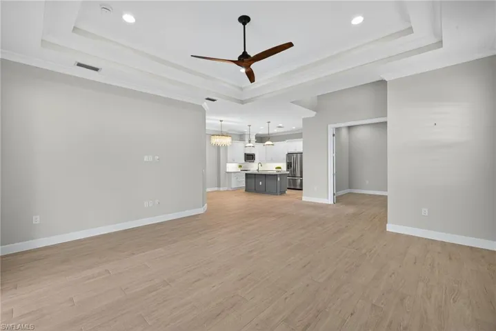 Unfurnished living room featuring a tray ceiling, a ceiling fan, light wood finished floors, a chandelier, and crown molding