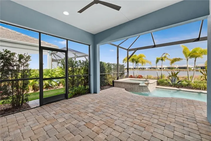 Unfurnished sunroom featuring a hot tub, a ceiling fan, a water view, and a patio