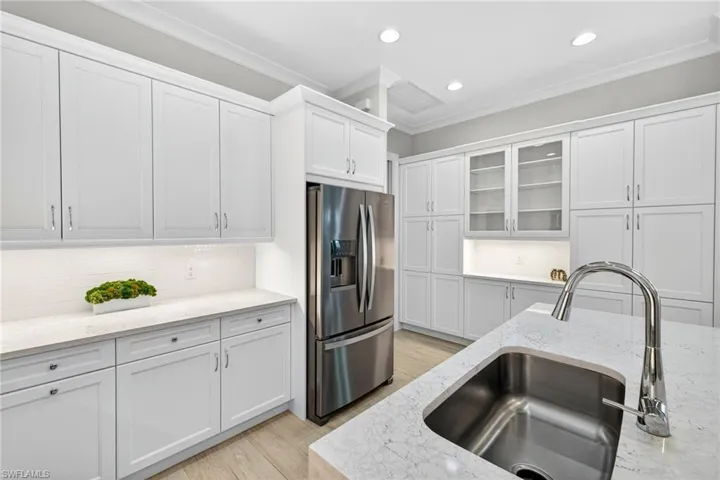 Kitchen with crown molding, stainless steel fridge with ice dispenser, tasteful backsplash, white cabinetry, and light wood-style floors