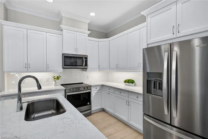 Kitchen with appliances with stainless steel finishes, backsplash, ornamental molding, light stone counters, and light wood-style floors