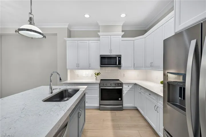 Kitchen with stainless steel appliances, backsplash, hanging light fixtures, ornamental molding, and white cabinets