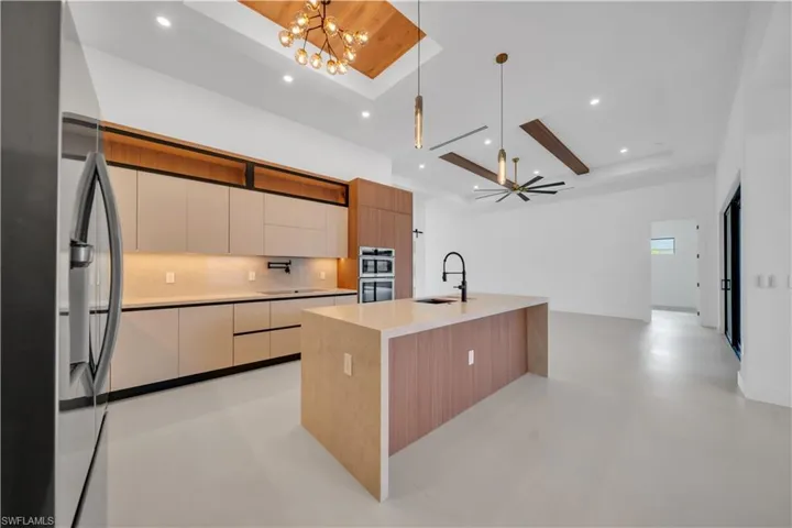 Kitchen with dual tone cabinetry, stainless steel appliances, modern cabinets, a kitchen island with sink, and light stone countertops