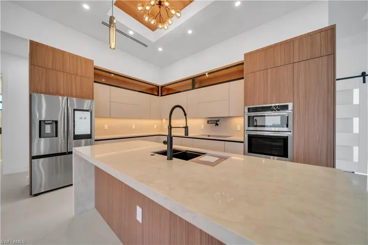 Two tone kitchen featuring modern cabinets, stainless steel appliances, light stone counters, tasteful backsplash, and dual tone cabinets