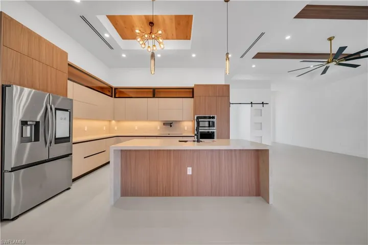 Kitchen with stainless steel appliances, modern cabinets, an island with sink, a barn door, and light stone countertops