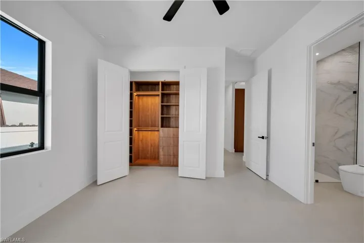 Unfurnished bedroom featuring a ceiling fan, finished concrete flooring, and ensuite bath
