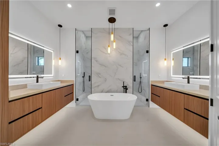 Bathroom with two vanities, a marble finish shower, a soaking tub, and recessed lighting
