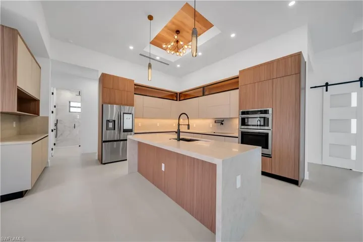 Kitchen with a barn door, stainless steel appliances, light stone counters, a center island with sink, and modern cabinets