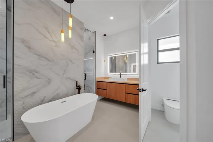 Full bathroom featuring vanity, a freestanding tub, a marble finish shower, concrete flooring, and recessed lighting