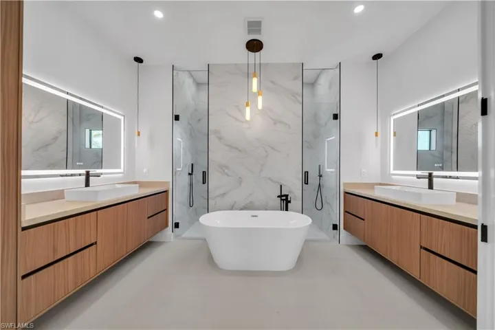 Full bathroom featuring two vanities, a marble finish shower, a freestanding bath, recessed lighting, and healthy amount of natural light