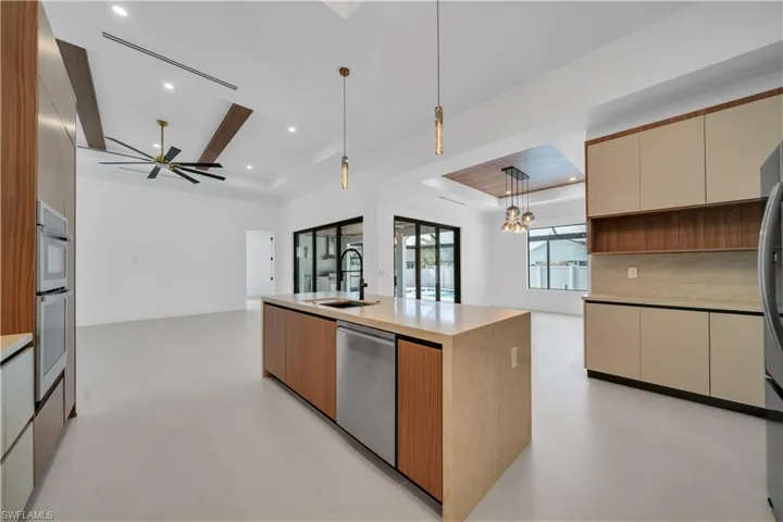 Two tone kitchen featuring a tray ceiling, open floor plan, stainless steel appliances, modern cabinets, and a center island with sink