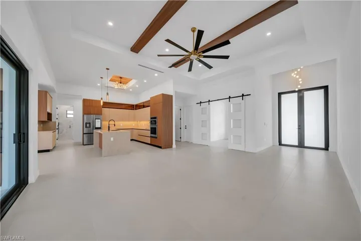 Unfurnished living room with a barn door, a ceiling fan, hanging lights, and plenty of natural light
