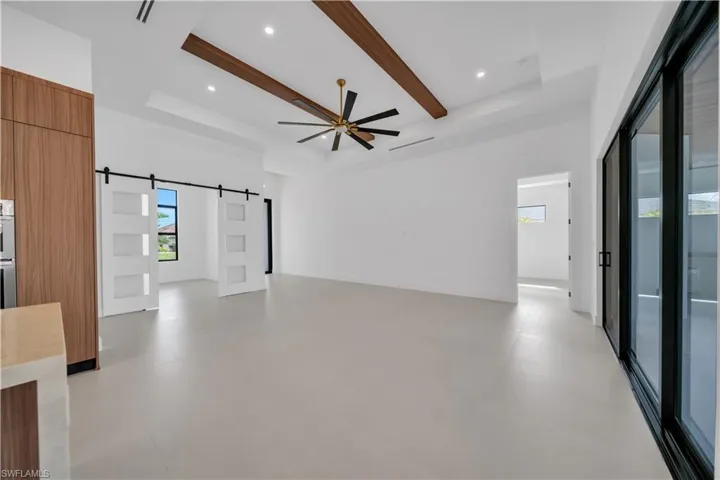 Unfurnished living room with a barn door, a ceiling fan, recessed lighting, and beamed ceiling