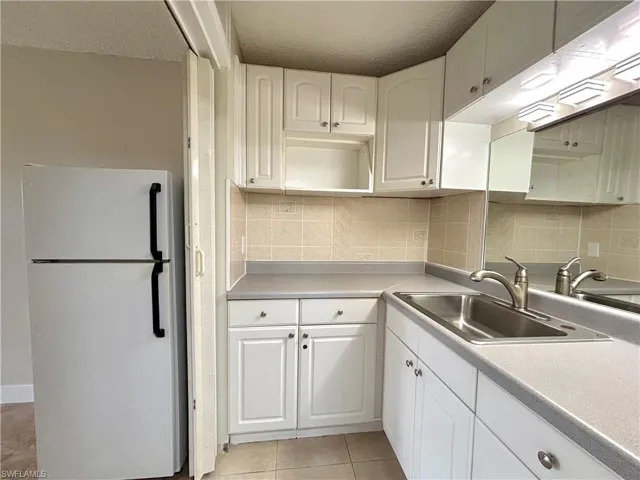Kitchen with freestanding refrigerator, tasteful backsplash, light countertops, white cabinets, and a textured ceiling