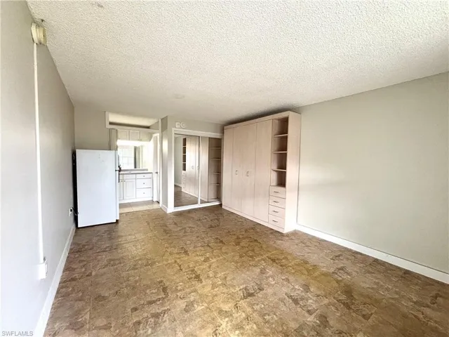 Unfurnished bedroom featuring freestanding refrigerator, a closet, and a textured ceiling