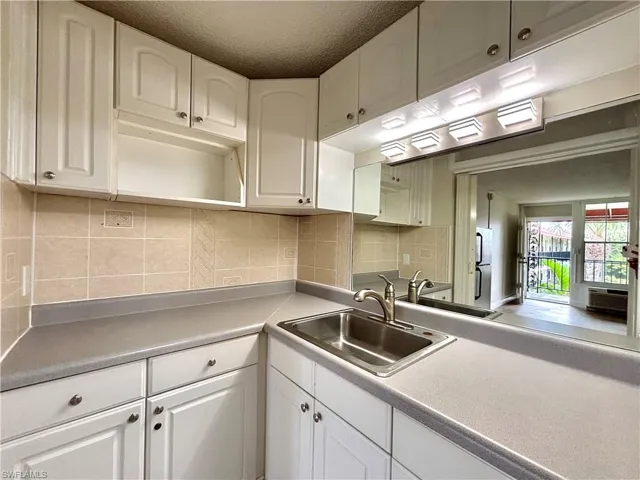 Kitchen featuring backsplash, white cabinets, light countertops, open shelves, and freestanding refrigerator