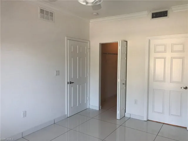 Spacious interior featuring white walls, tile flooring, and crown molding