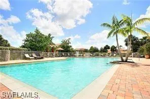 Resort-style pool area featuring a large swimming pool, paver deck, mature palm trees, perimeter fencing, and abundant natural light