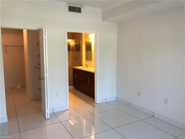 Bright interior space featuring large format white tile flooring, white walls, and crown molding
