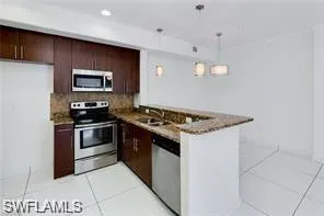 Kitchen featuring dark wood cabinetry, stainless steel appliances, granite countertops, and a peninsula with breakfast bar seating