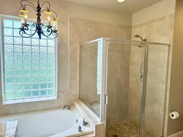 Bathroom featuring plenty of natural light, an inviting chandelier, and shower with separate bathtub