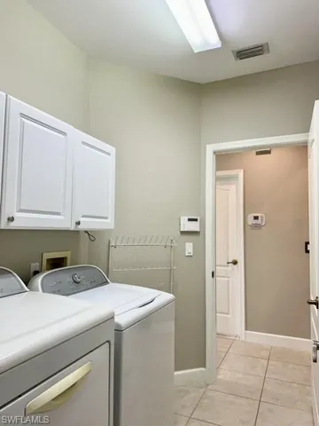 Washroom with cabinets, light tile patterned floors, and washing machine and dryer