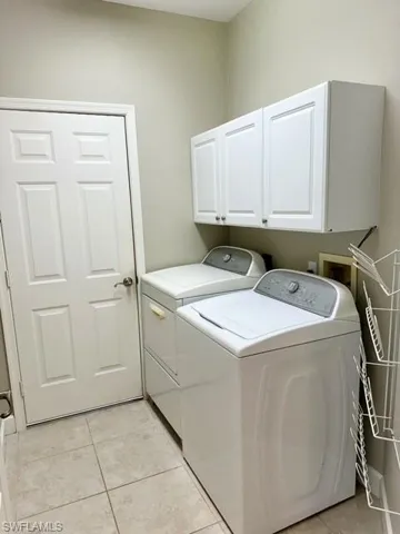 Clothes washing area featuring light tile patterned floors, cabinets, and washing machine and dryer