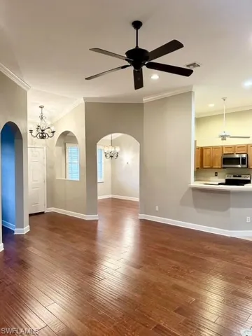 Unfurnished living room featuring dark wood-type flooring, ceiling fan with notable chandelier, and crown molding