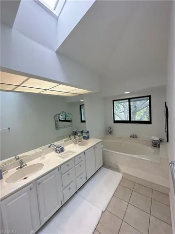 Full bathroom featuring a skylight, light tile patterned floors, a garden tub, double vanity, and vaulted ceiling